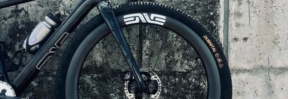 Front of a dark gravel bike with an ENVE carbon rim and Continental Dubnital tire against a concrete wall