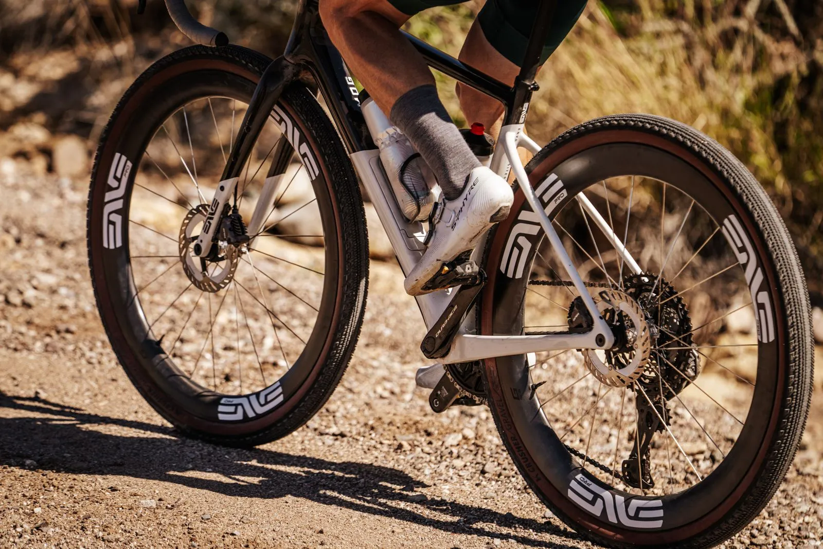 Rider on a white gravel bike with ENVE wheels crossing a dusty rocky track