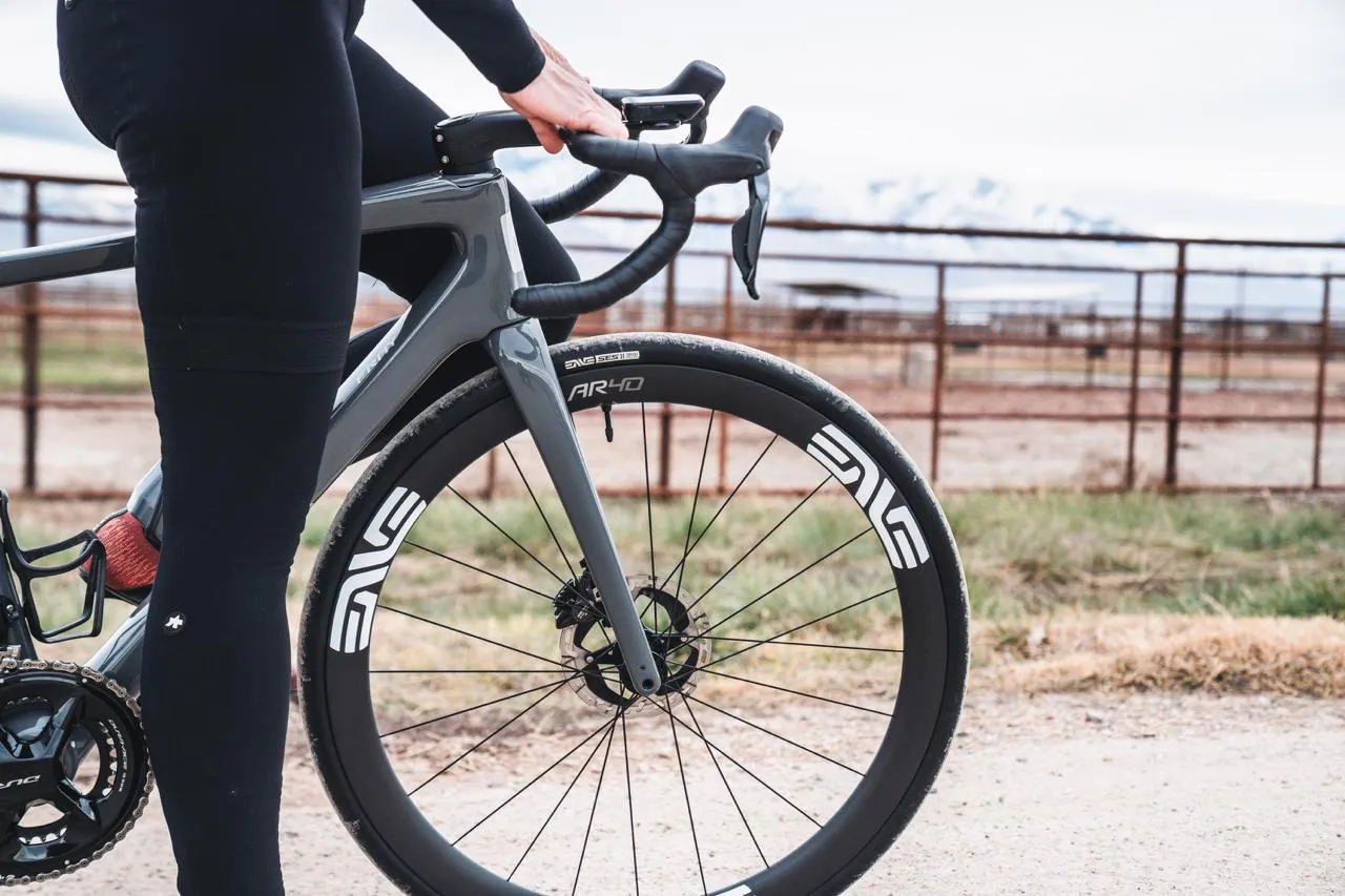 Rider in black kit standing over a grey gravel bike with ENVE wheels beside a ranch fence